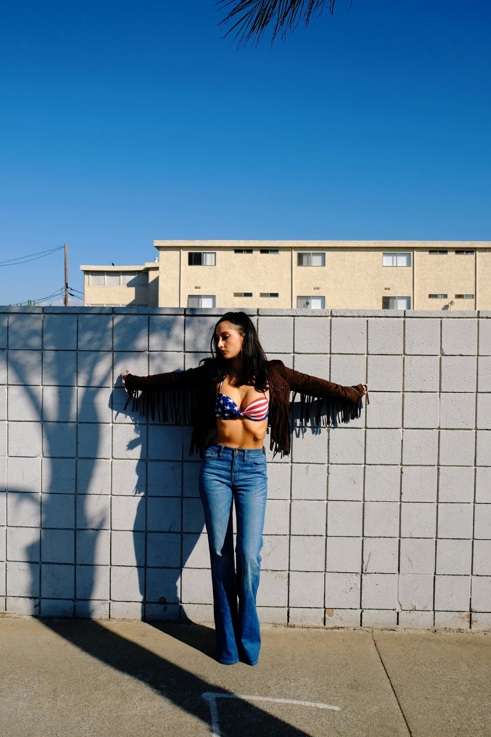 woman in blue denim jeans standing beside white concrete building during daytime